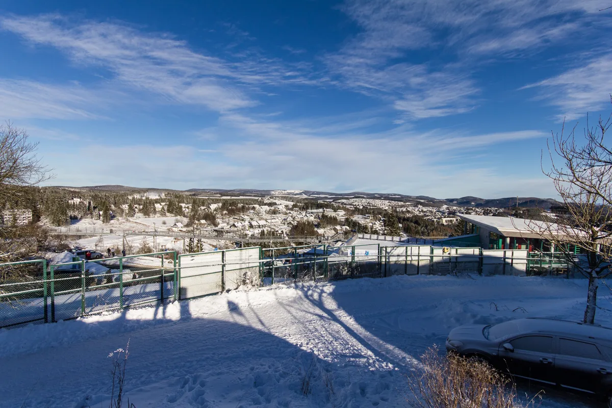 Verschneiter Winterort mit bewaldeten Hügeln unter blauem Himmel